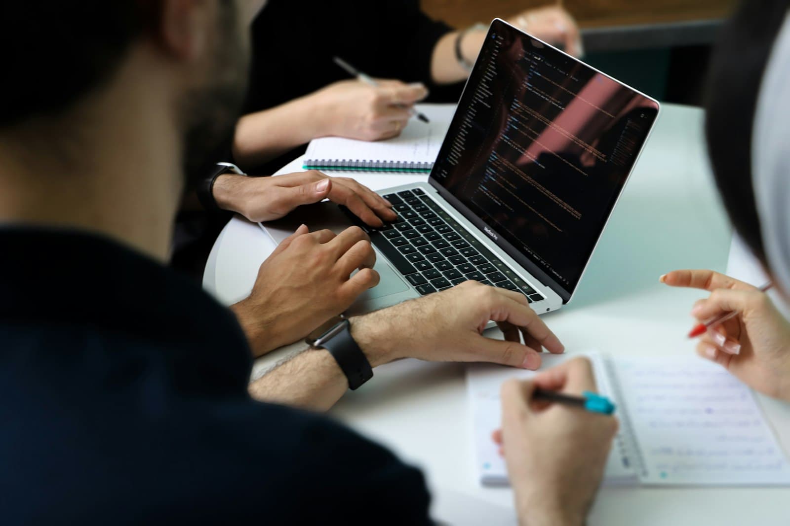 Illustrationsfoto: mehrere Personen um einen Laptop und Notizen versammelt, in einer Arbeitssitzung.
